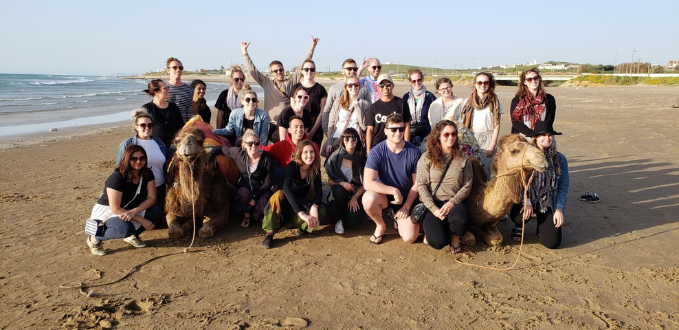 Group posing with camels on a beach.