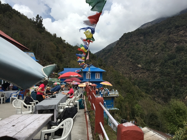 Tourists dining on a patio with prayer flags and mountain views.