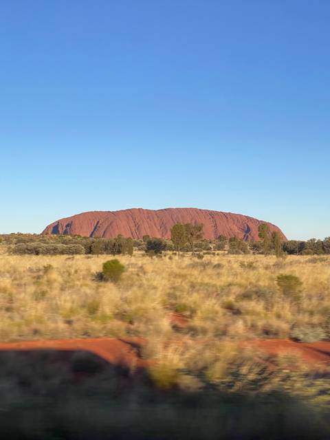Red rock formation and grassland under a blue sky.