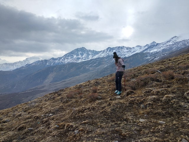 A hiker walking in the mountains with snowy peaks in the background.
