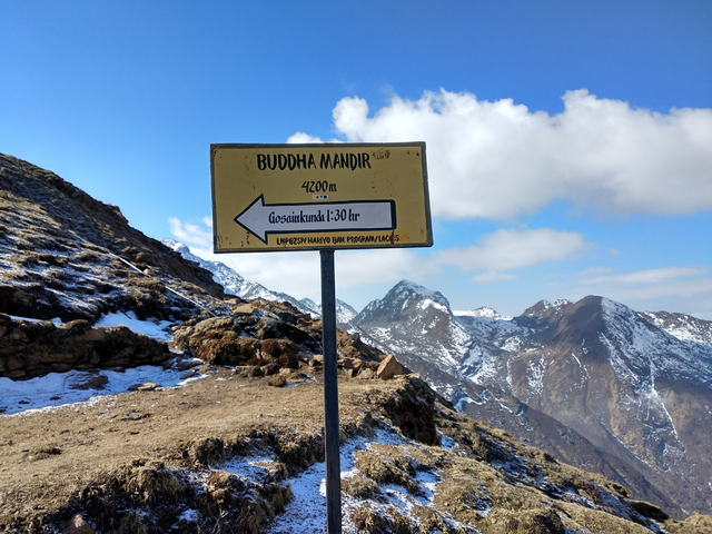 A signpost at Buddha Mandir with snow-covered mountains in the background.