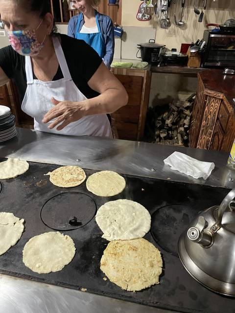 Cooking tortillas on a stovetop with a person nearby.
