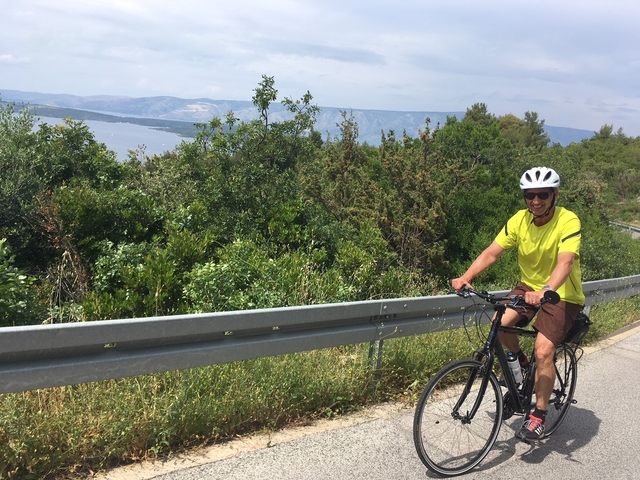 A man cycling along a road with a scenic view of the sea.