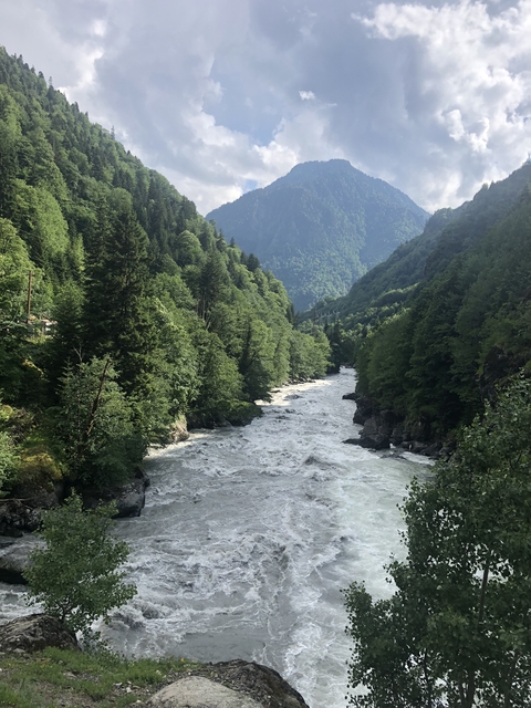 A river flowing through a valley surrounded by lush green forest and mountains.