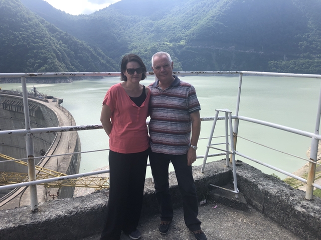       Two people posing on a balcony overlooking a reservoir.
  