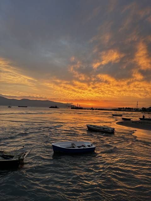 Silhouette of boats at sunset with orange sky and water reflection.