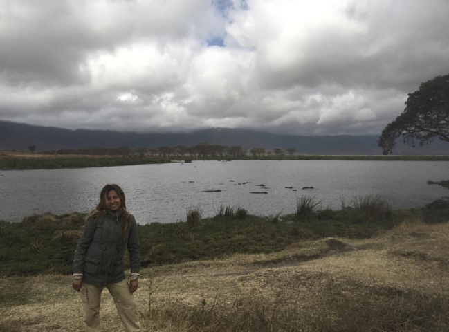 A woman smiling near a water body under cloudy skies.