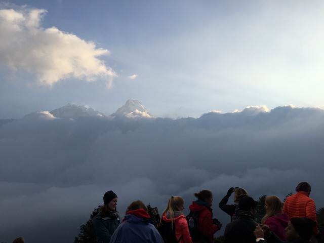 People observing a scenic view of mountains peeking through clouds.