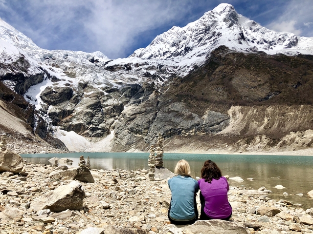 People sitting by a turquoise glacial lake surrounded by mountains.