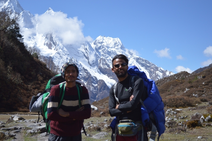 Two men in front of snowy mountains, dressed for hiking.