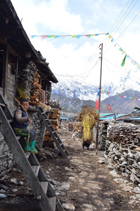 Boy sitting in a village with snowy mountains in the background.