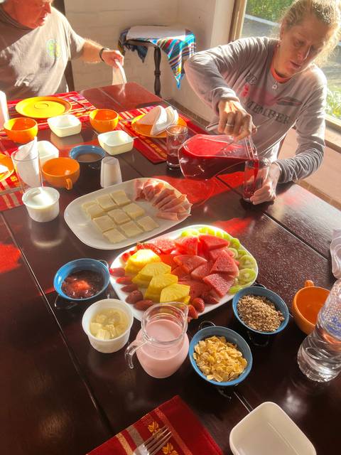 A table with plates of fruit and juice, with people serving.
