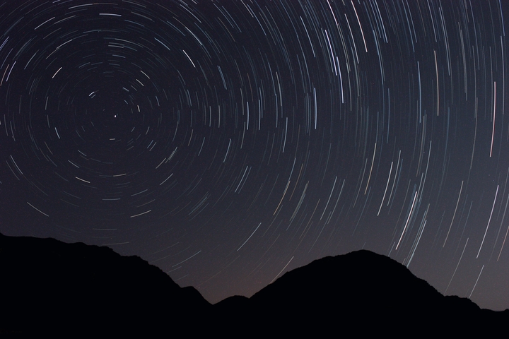       Night sky with star trails above silhouette of hills.
  