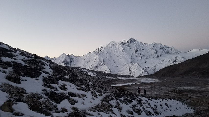 Snowy mountain landscape with two small figures walking.