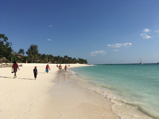 Beach with people walking and boats in the water.