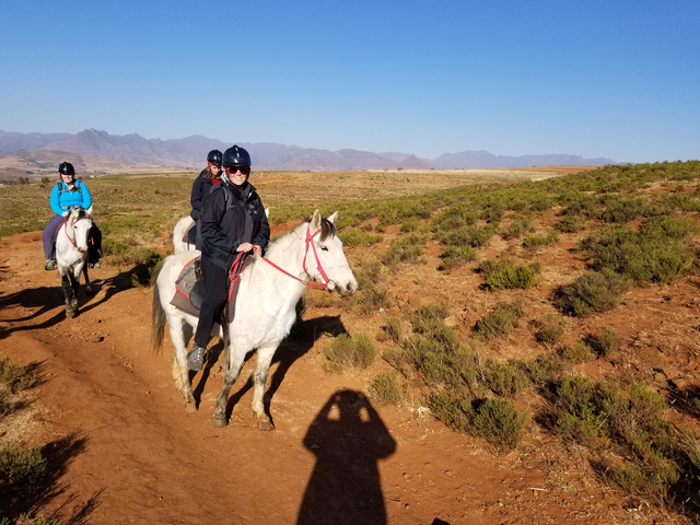 Two people on a horseback riding trail with scenic mountains in the background.