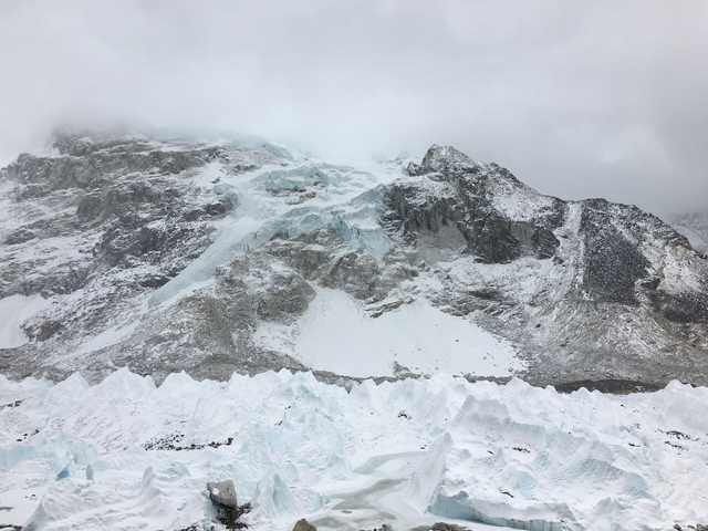 Snow-covered rocky mountain under a cloudy sky.
