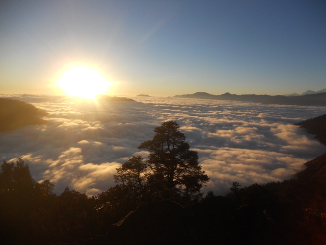 Sunrise over a sea of clouds with mountain silhouettes.