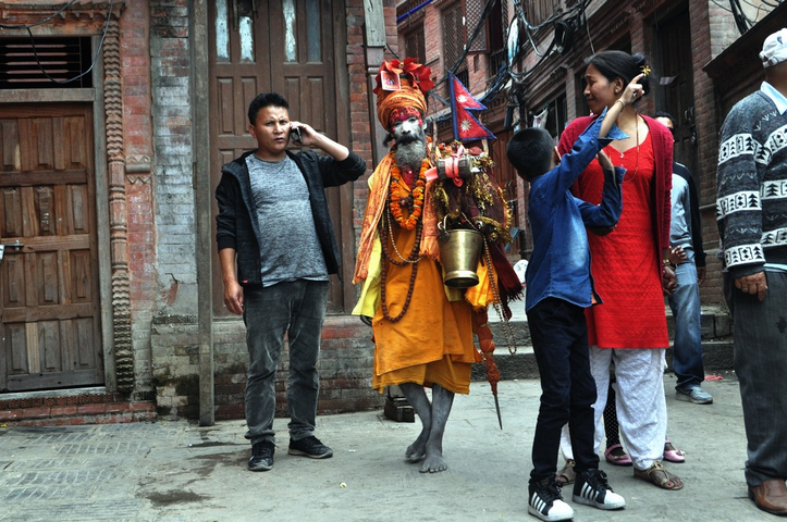 Individuals on a street, one dressed as a traditional sadhu.