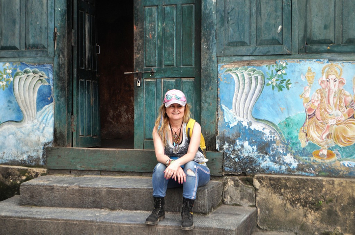 Person seated in front of a vibrantly colored wall with paintings.
