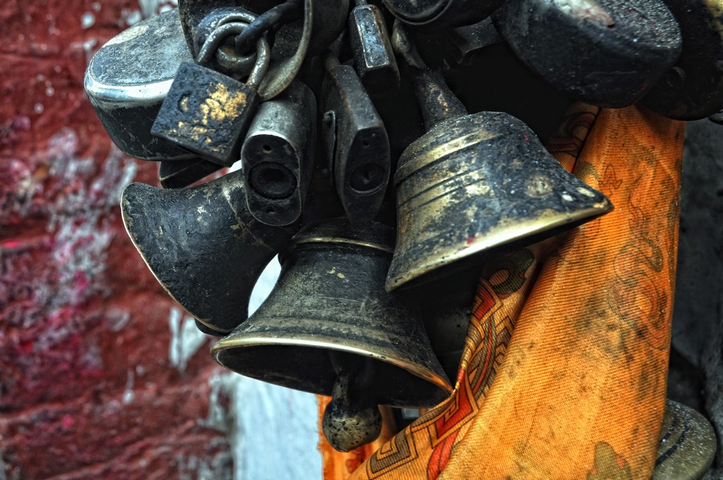 Close-up of hanging bells with a colorful fabric in the background.