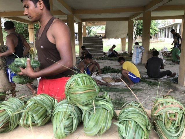 People working and weaving baskets in an open structure.