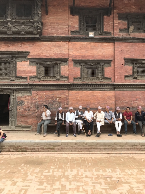 Group of men sitting in front of a traditional brick building.