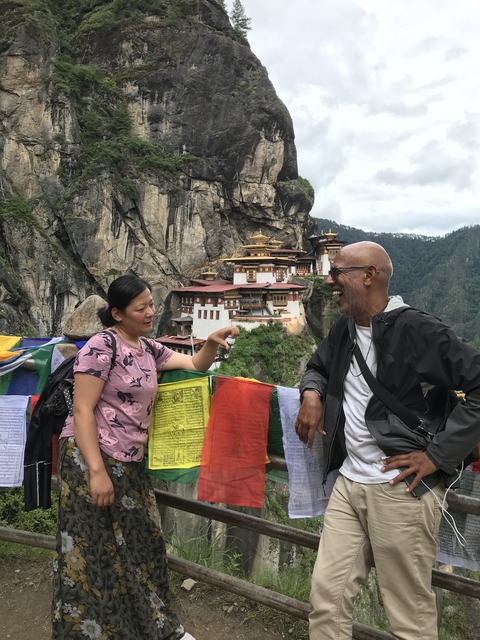 People talking in front of Paro Taktsang nestled in the mountains.