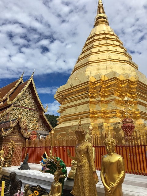 Golden stupa and adorned temple with intricate carvings against a blue sky.