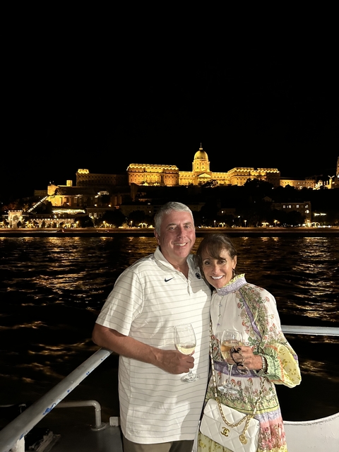       A couple posing with an illuminated building in the background at night.
  