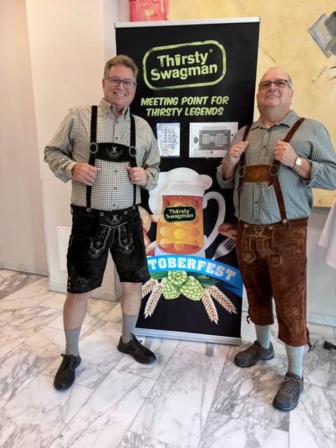 Two men in traditional outfits by a festival poster.