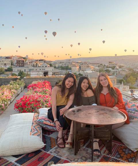       Three women sitting on a terrace with hot air balloons in the sky.
  