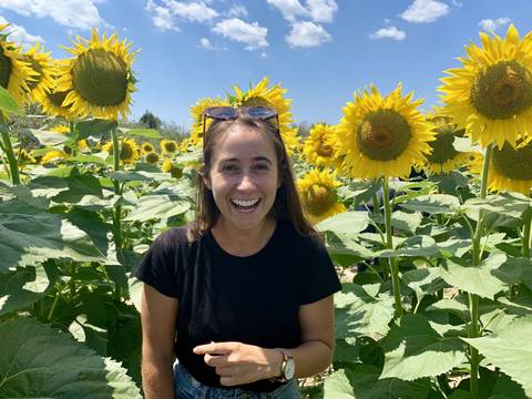       A smiling woman surrounded by sunflowers.
  
