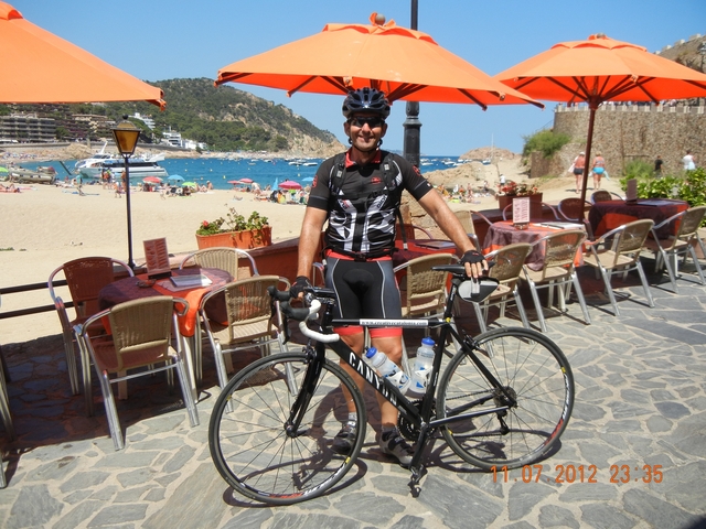 Cyclist posing with a bicycle by the beach with umbrellas in the background.