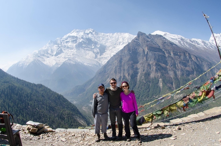       Three people in front of snow-capped mountains and prayer flags.
  