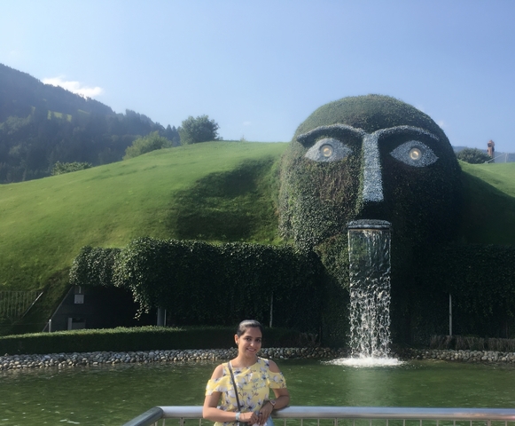 Large grass-covered sculpture with a fountain, woman posing in front.