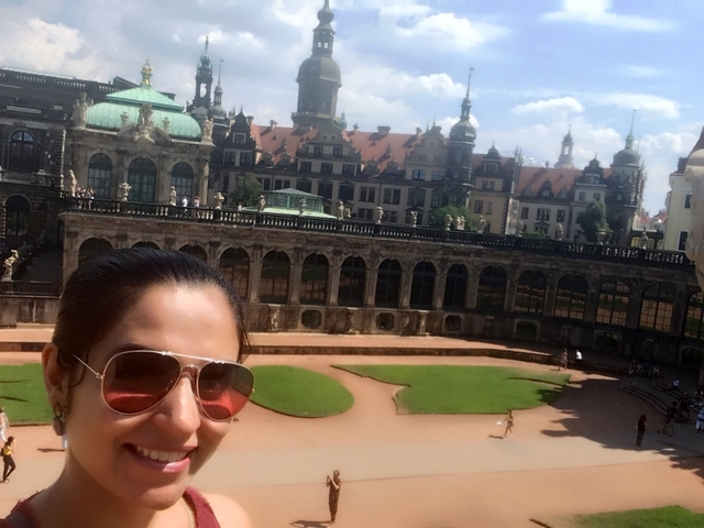 Woman with sunglasses at a tourist site with historic architecture.