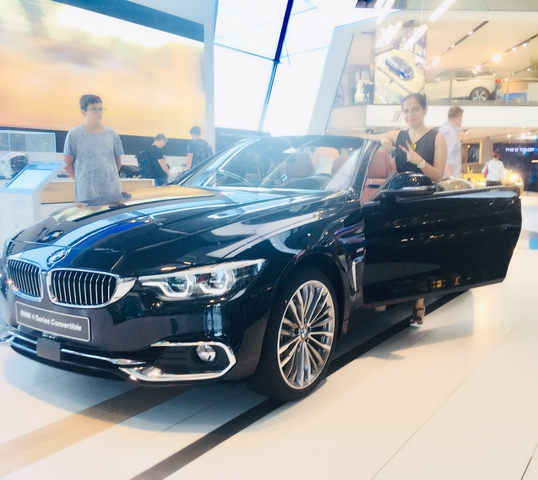 Woman standing beside a luxury car in an indoor showroom.
