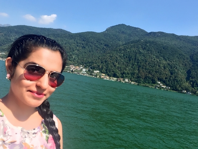 Selfie of a woman by a large lake with hills in the distance.