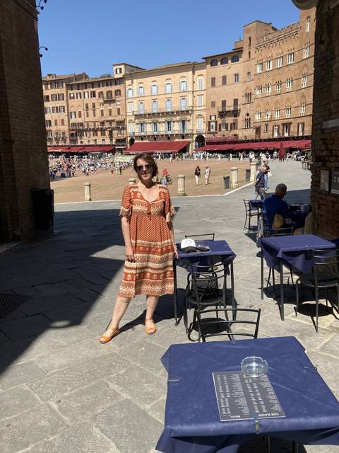 Person posing in a busy piazza with historic buildings.