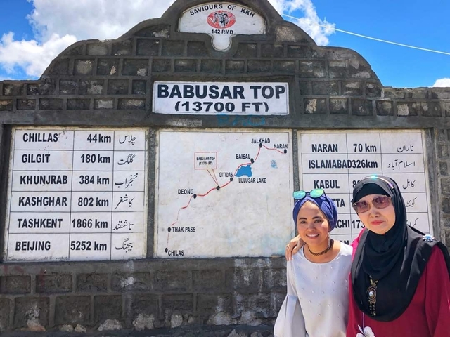       Two women posing in front of a signboard at a high elevation.
  