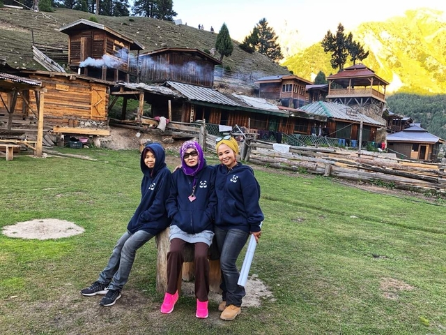       Three people seated outside traditional wooden houses.
  