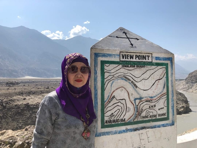       Woman standing beside a viewpoint sign with mountains behind.
  