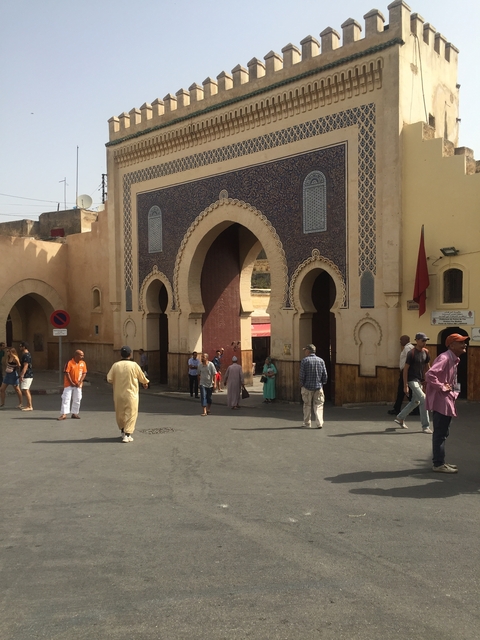       Busy street scene with people near a large gate.
  