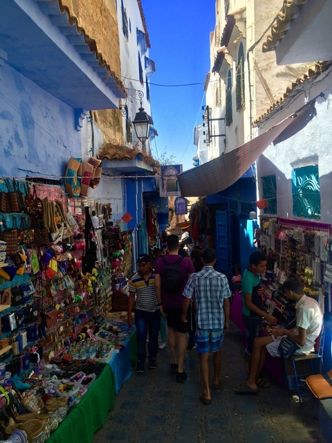       Crowded market scene in a narrow street with vibrant blue walls.
  