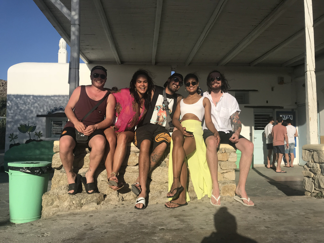       Five people sitting on a ledge enjoying the sun.
  