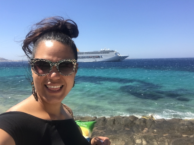       Woman posing with the ocean and a cruise ship in the background.
  