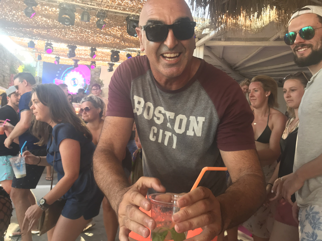       Man holding a drink at an outdoor party with people around.
  