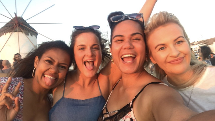       Four friends taking a cheerful selfie with a windmill in the background.
  