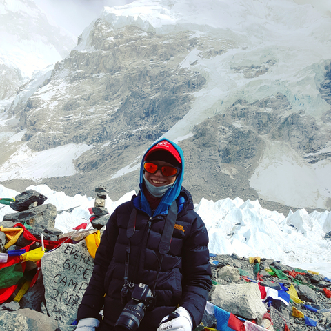       Person with trekking gear posing with snowy mountains in the background.
  